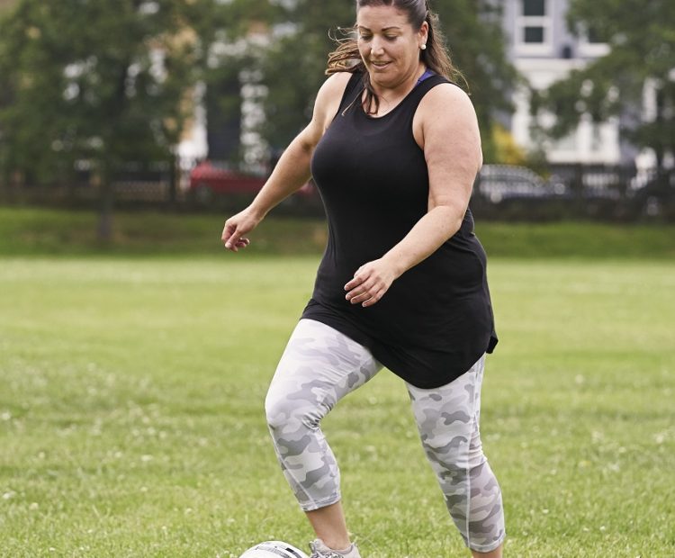 middle aged woman plays football in park